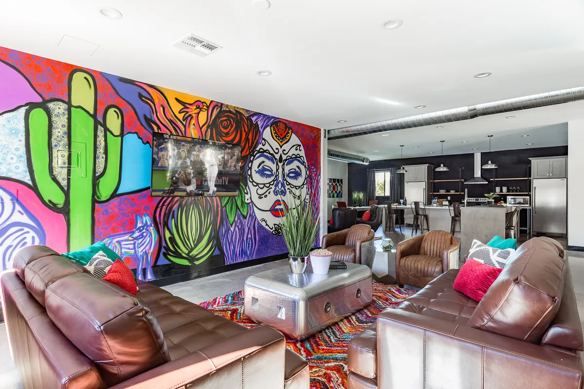 A lively living space with leather sofas, a colorful mural on the wall, a coffee table, and a television. The setting feels energetic and perfect for larger groups or families to socialize, watch TV, or play games together.