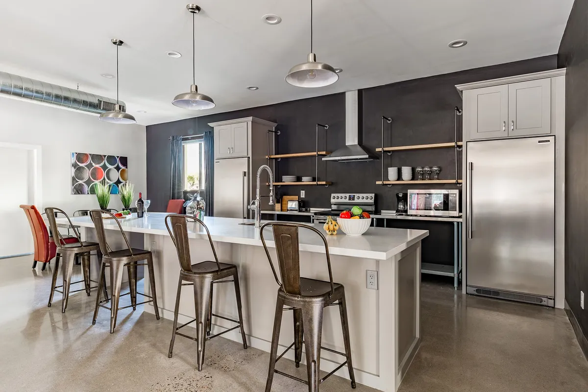 A sleek and modern kitchen with a spacious island countertop, stainless steel appliances, and well-organized open shelves holding kitchenware. Bright lighting and a lively atmosphere suggest a space ideal for entertaining or cooking together.