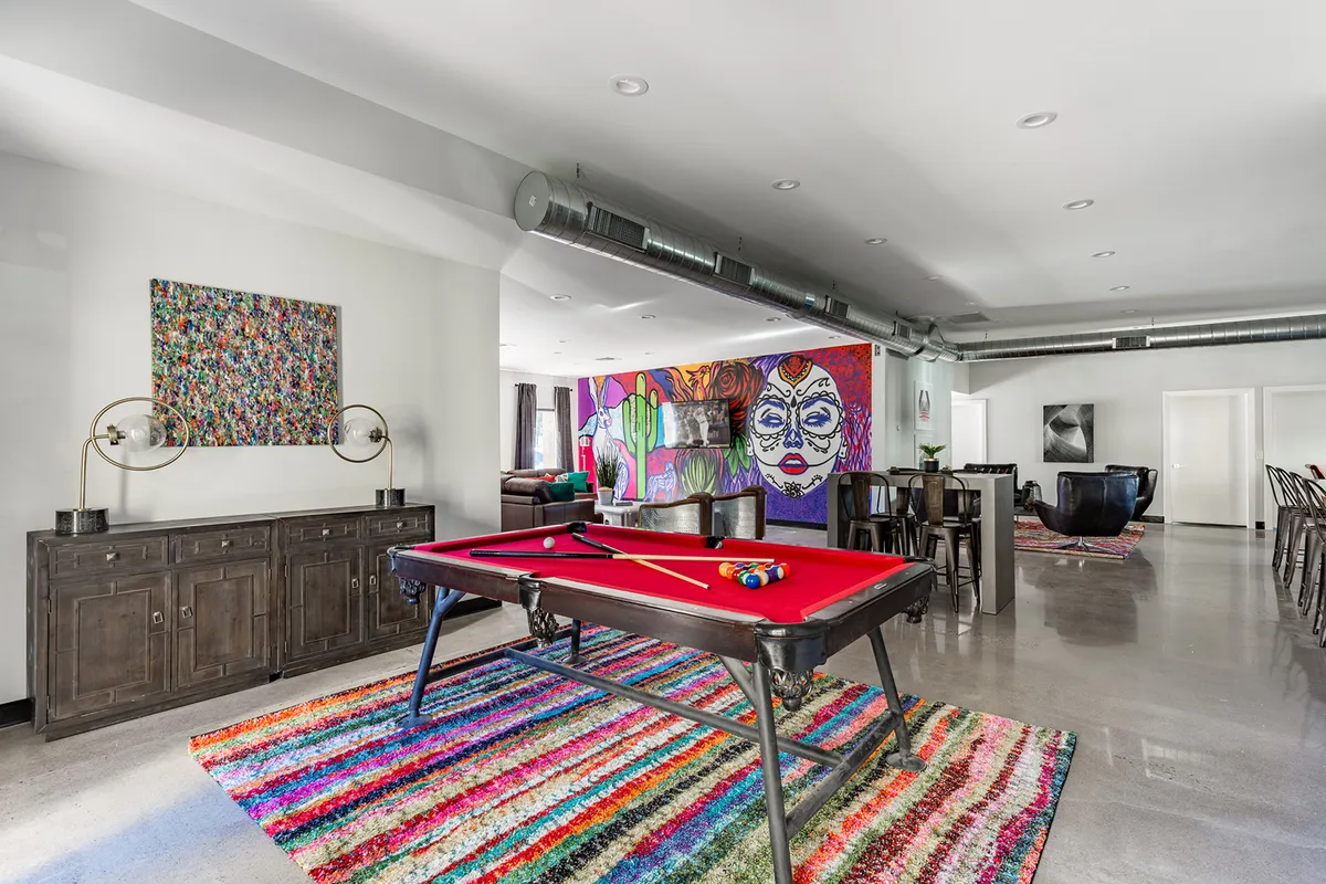 This image captures a vibrant game lounge featuring a pool table at the center, a colorful area rug, a large wall mural, and art pieces on the wall. The playful decor and ample space make it ideal for entertaining guests and hosting game nights.