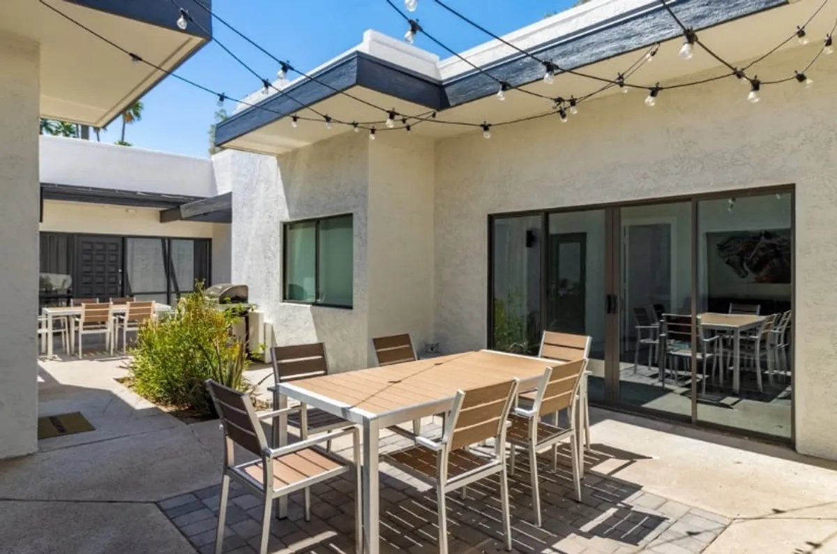 This image showcases an outdoor dining table set beneath string lights, surrounded by lush greenery and large sliding glass doors that connect the patio to the interior. The festive setup suggests an ideal spot for group gatherings, evening celebrations, or relaxed coffee moments while basking in Arizona’s signature sunshine.
