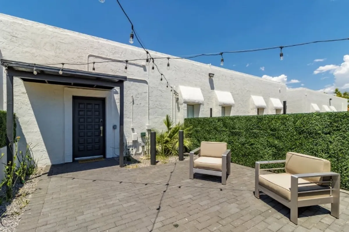 An exterior scene featuring a cozy front seating area framed by a green hedge and twinkling hanging lights. The space is perfect for both sunny afternoons and evening gatherings, illustrating the variety of outdoor relaxation options available.