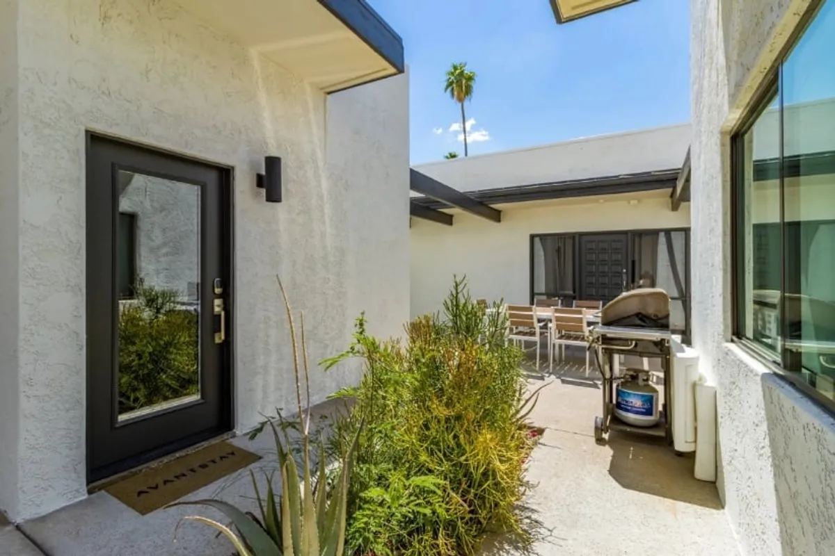 This image features the front door of a home with an outdoor dining area, grill, and potted plants, creating an inviting patio space perfect for hosting gatherings or enjoying meals outside. The scene captures the essence of a welcoming exterior and the potential for communal activities.