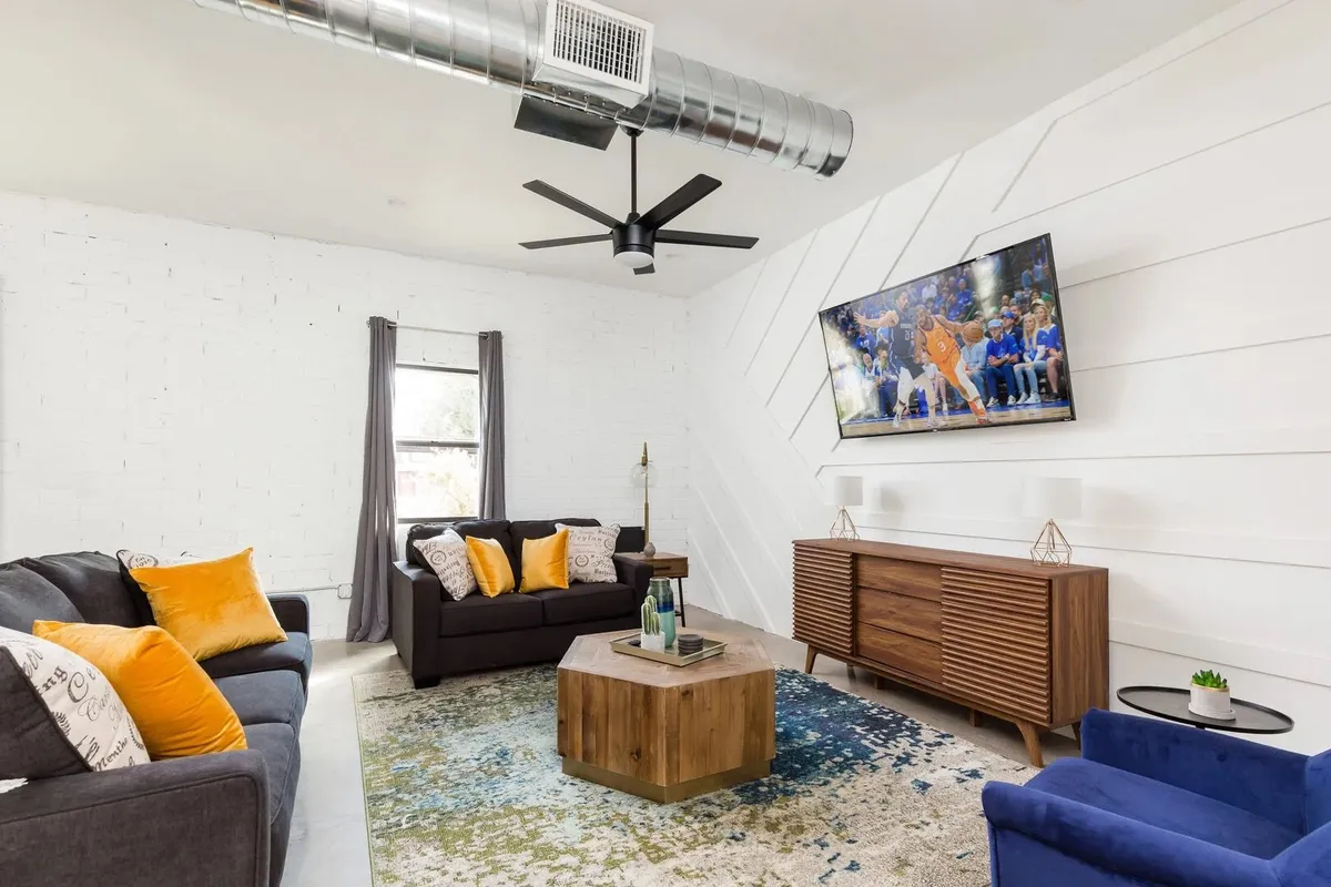 A cozy main living area with a plush sofa accented by yellow cushions, a wooden coffee table, and a television mounted on the wall. The contemporary decor and inviting setup create an ideal spot for movie nights or planning group adventures.