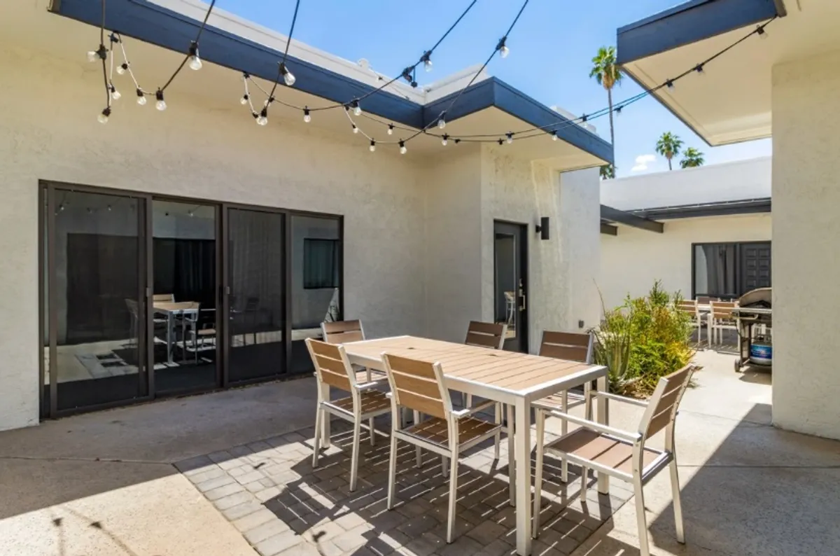 An inviting outdoor dining space with a table set beneath string lights, surrounded by lush greenery. The cozy setting evokes a cheerful, festive mood for al fresco meals.